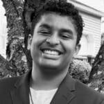 Smiling young person in front of a tree.