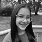 Smiling girl with glasses outdoors in black and white.